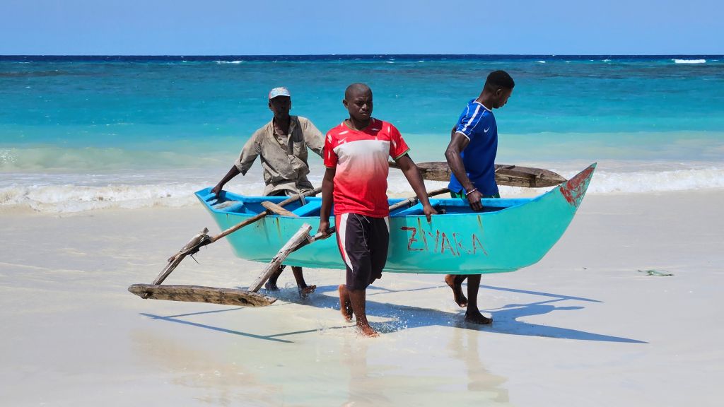 Fishermen dragging a wooden pirogue onto Chomoni Beach, Comoros